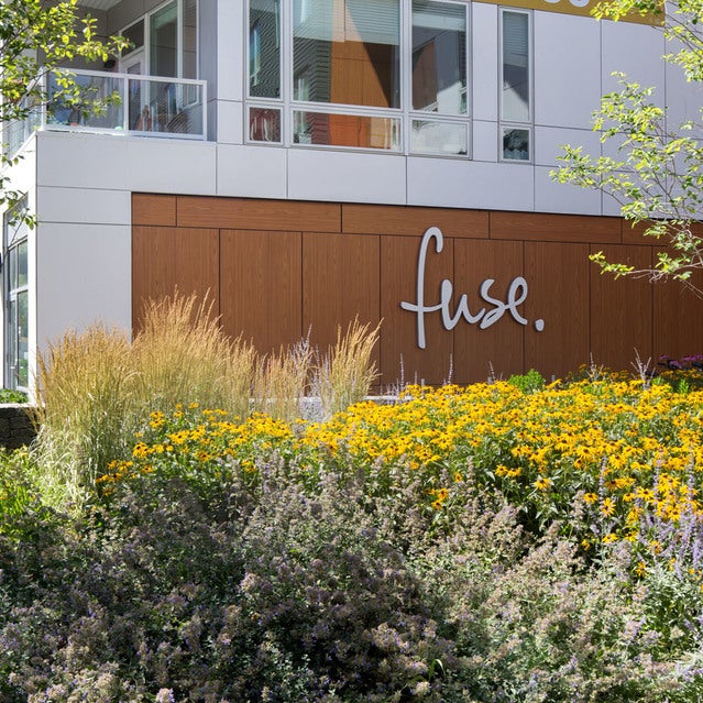 Fuse Cambridge Apartments - view of front entrance surrounded by trees & flowers